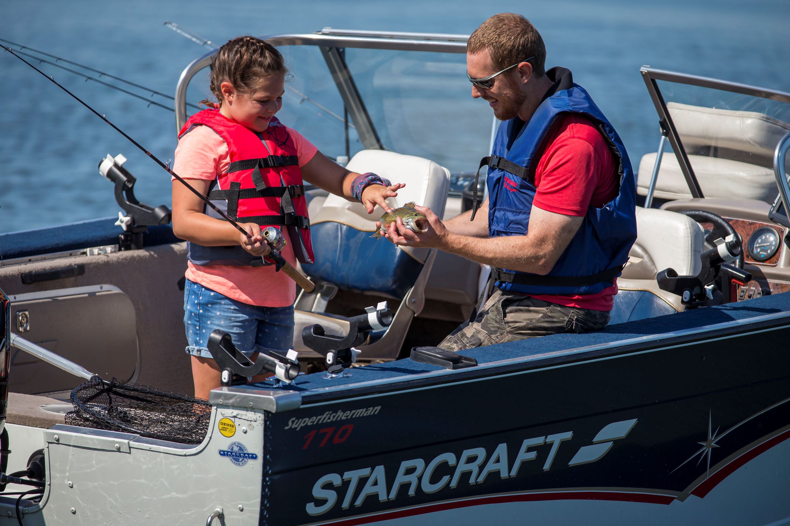 Father and daughter on boat in water with fish on fishing line.