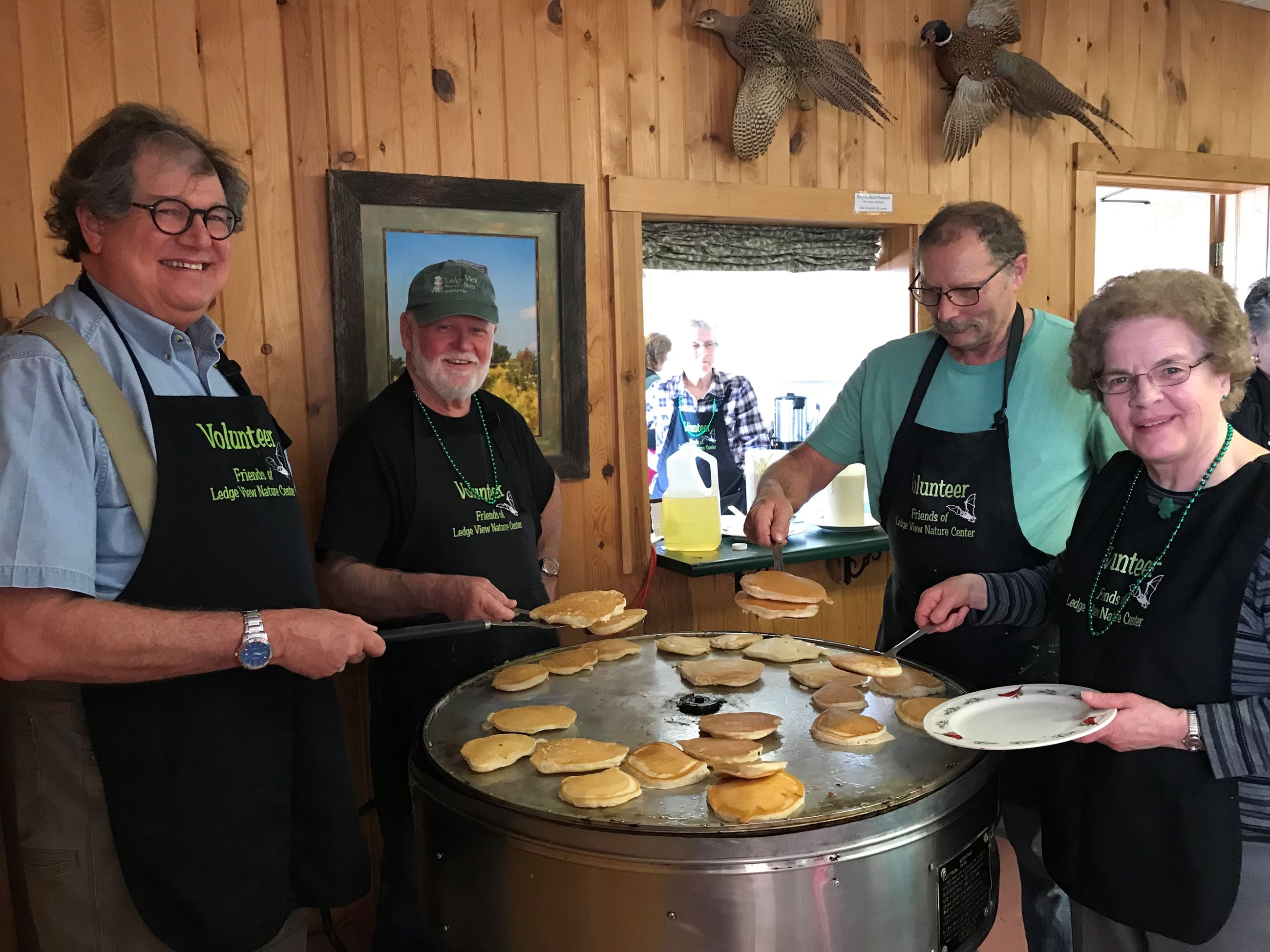 4 people cooking pancakes on a large round cooker